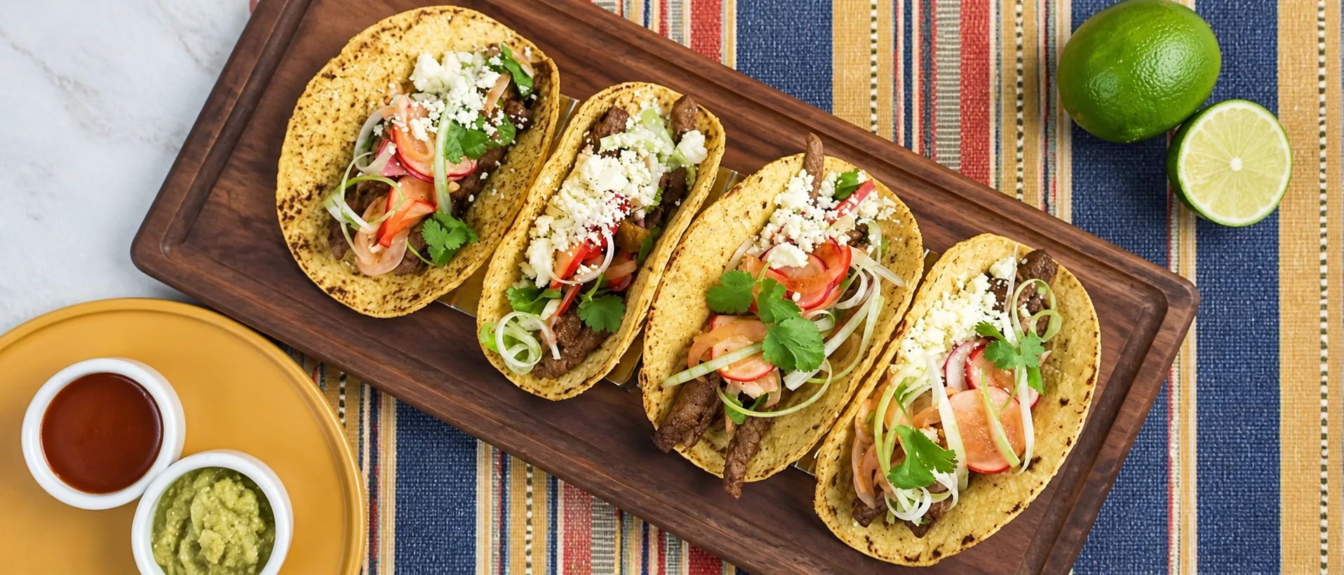 Four folded corn tortilla tacos with fresh toppings on a wooden serving board