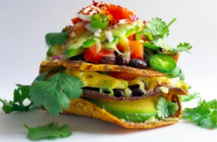Three crisp corn tortilla layers filled with black beans, avocado and cheddar, topped with fresh vegetables and sour cream