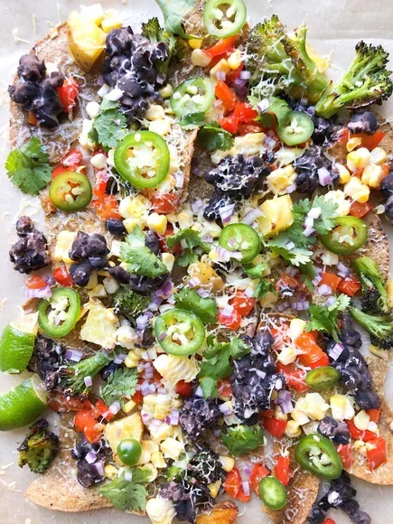 Sheet-pan nachos on crisp corn tortillas, topped with beans, fresh vegetables, and herbs